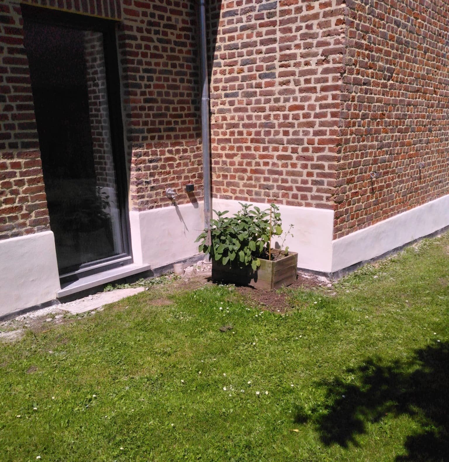 Soubassement enduit d’une maison en briques, angle et baie